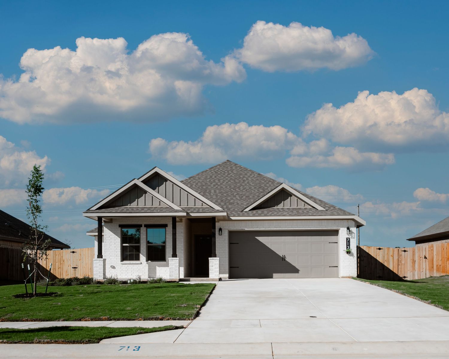 Five modern suburban homes with white exteriors and attached garages line up against a bright blue sky with puffy clouds.