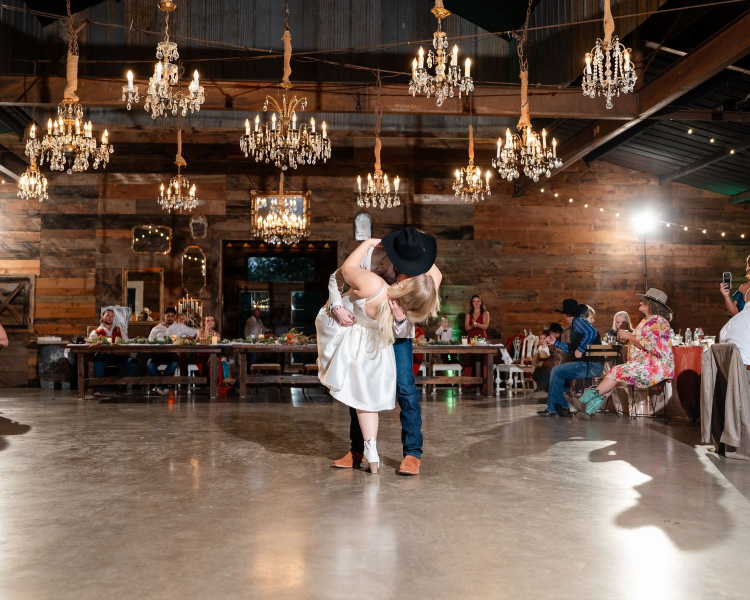 Elegant barn reception venue with multiple crystal chandeliers and string lights.