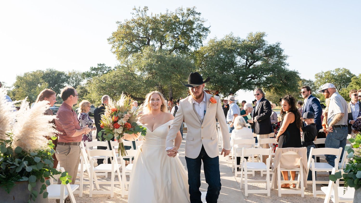 Panoramic view of wedding guests seated in white chairs at an outdoor ceremony venue.