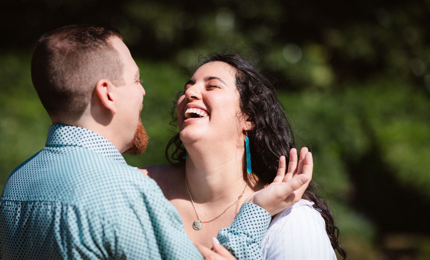 A couple laughs together during a romantic outdoor photoshoot in a green garden setting.