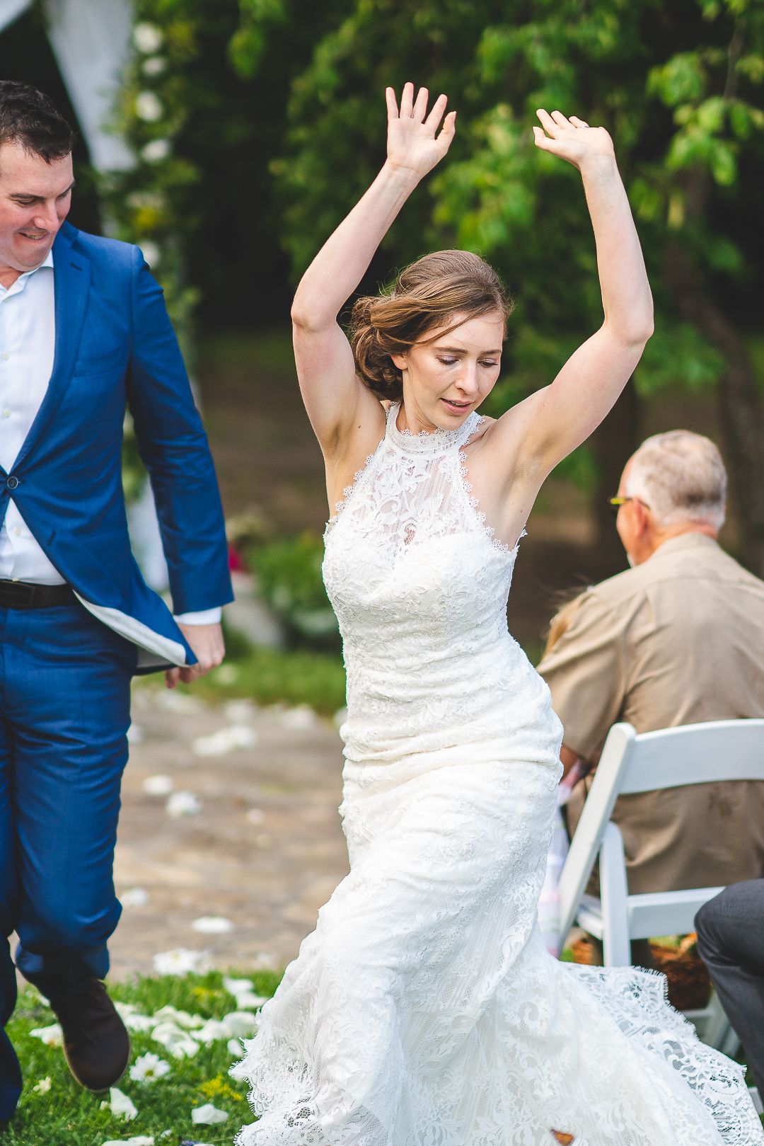 Bride in lace dress celebrating joyfully during outdoor wedding festivities.