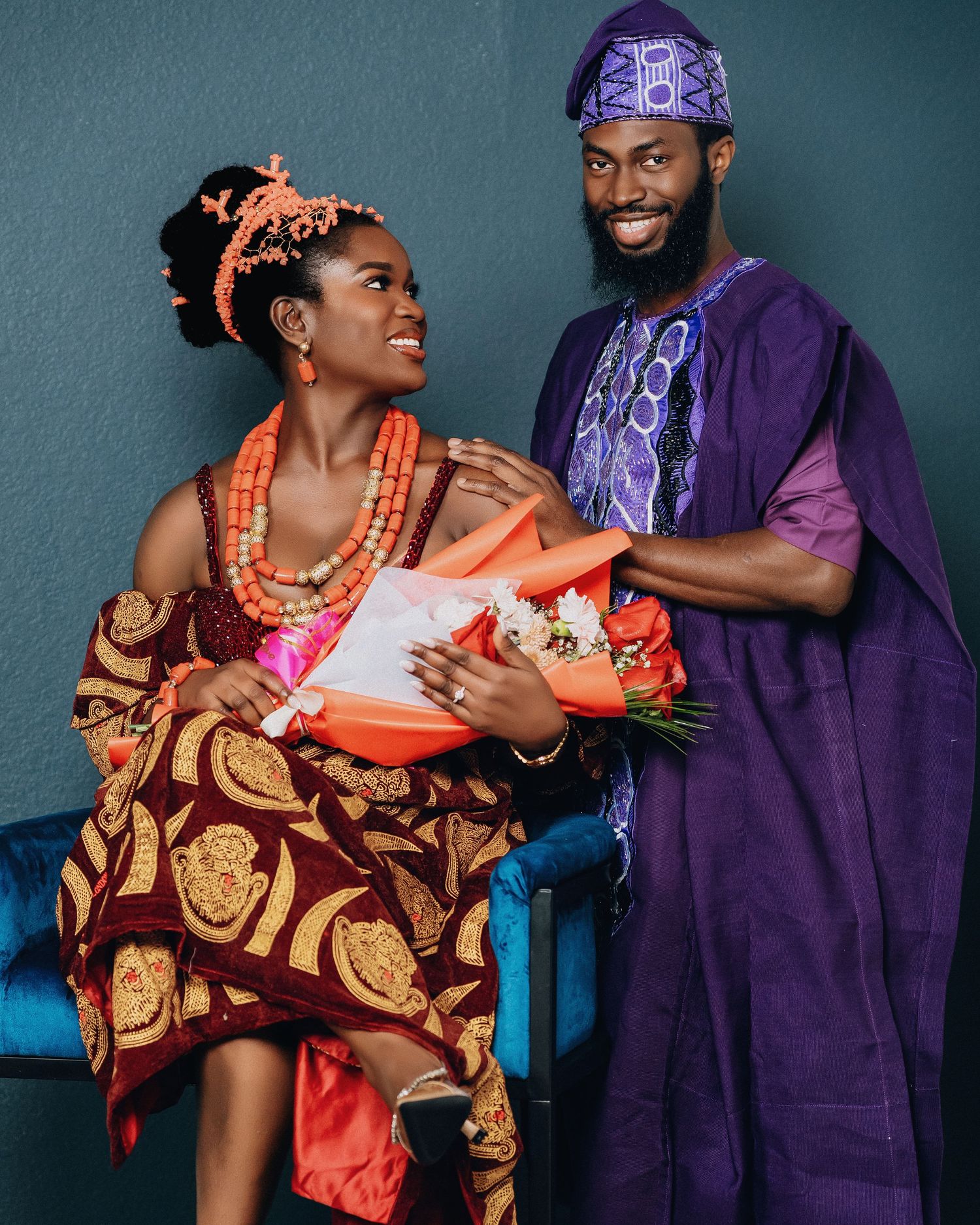 Couple in Nigerian traditional wedding attire with purple and orange accents pose playfully together.