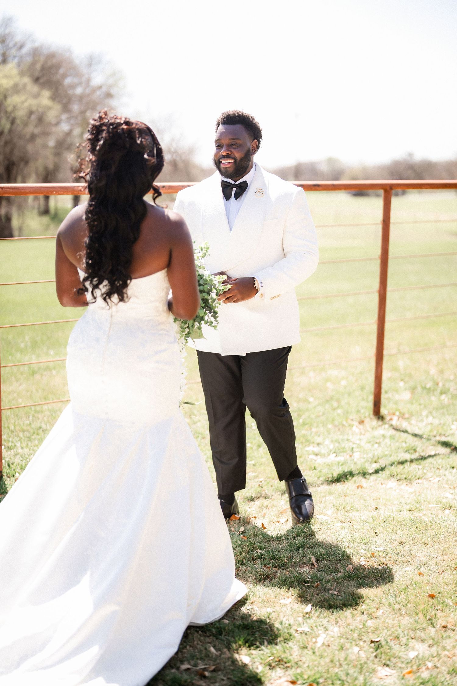 Wedding couple shares romantic moments in a sunlit field with wooden fencing.
