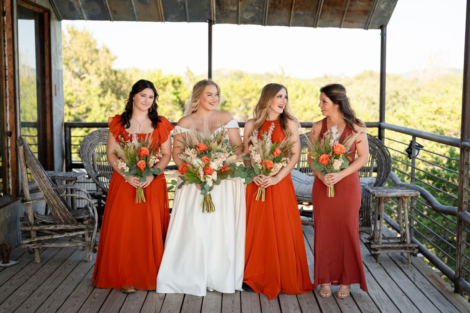 Wedding party in red and white dresses poses on outdoor deck.