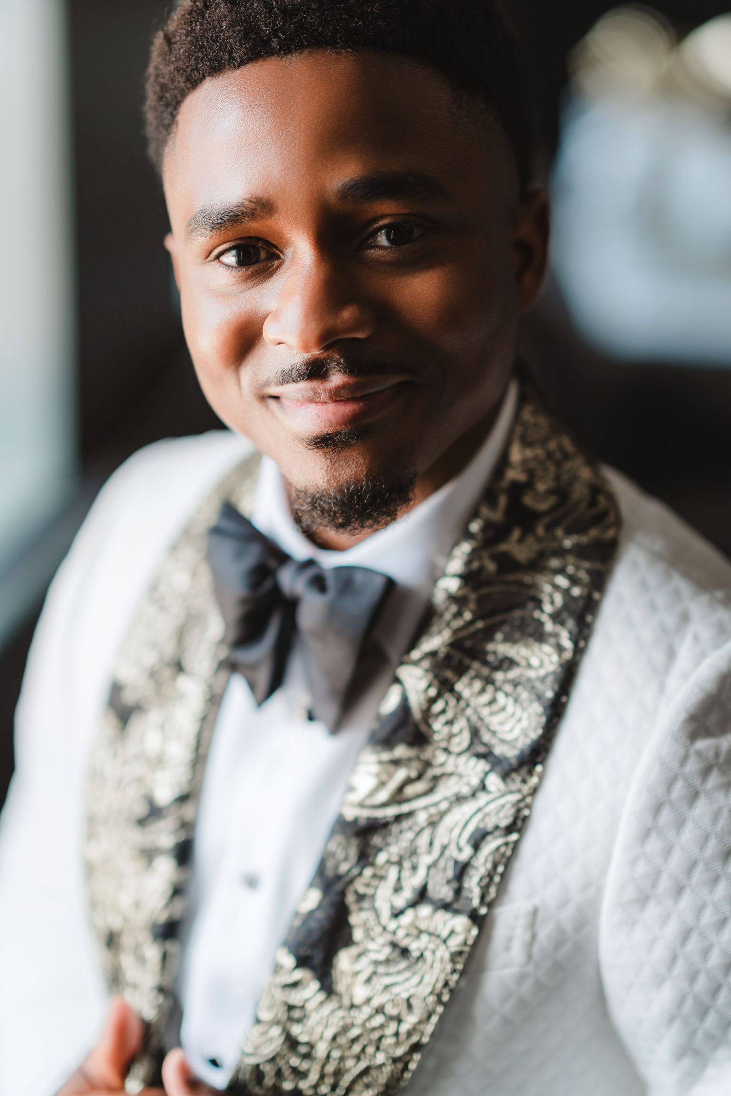 Stylish groom wearing a white textured tuxedo jacket with paisley lapels and black bow tie.