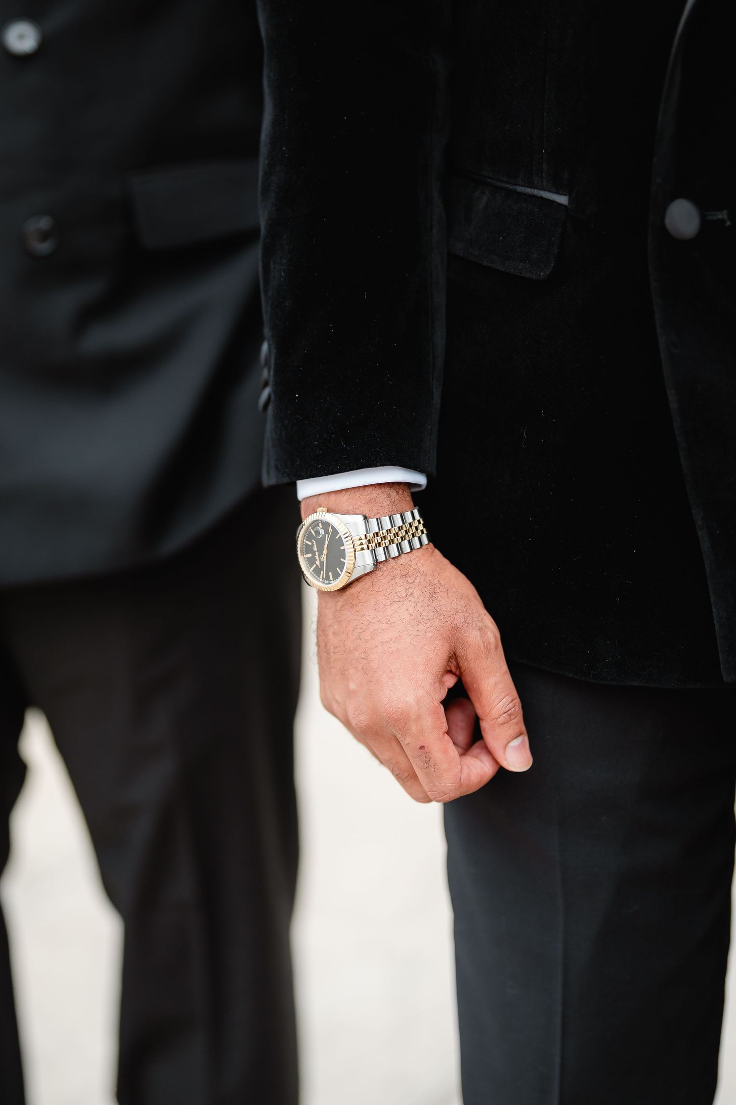 Close-up detail shot of groom's formal black tuxedo and hands.