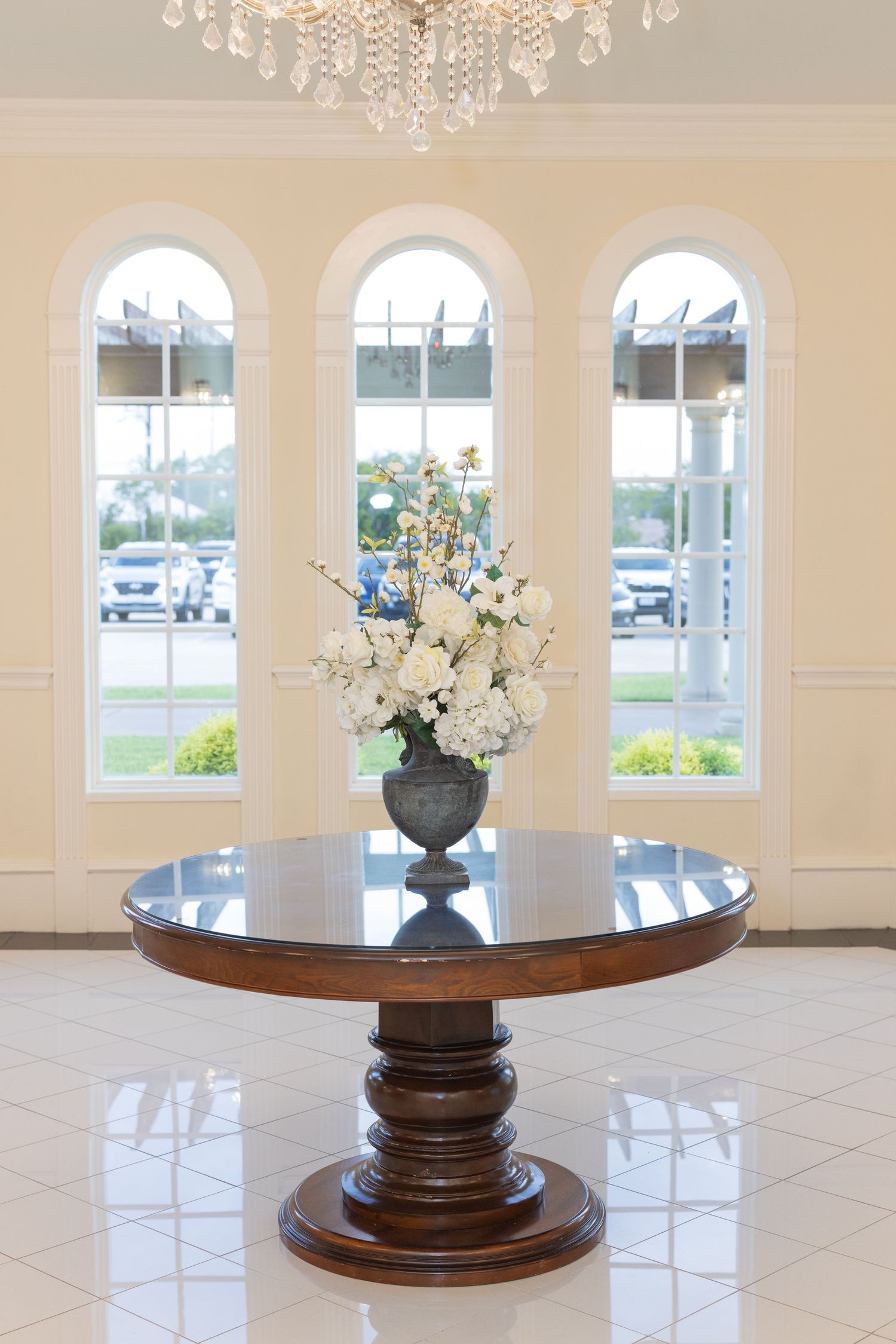 Elegant wedding venue interior with crystal chandelier, arched windows and decorative floral centerpieces.