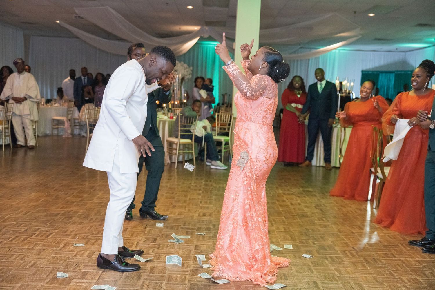 Wedding guests dancing and celebrating on dance floor with orange-clad bridesmaids.