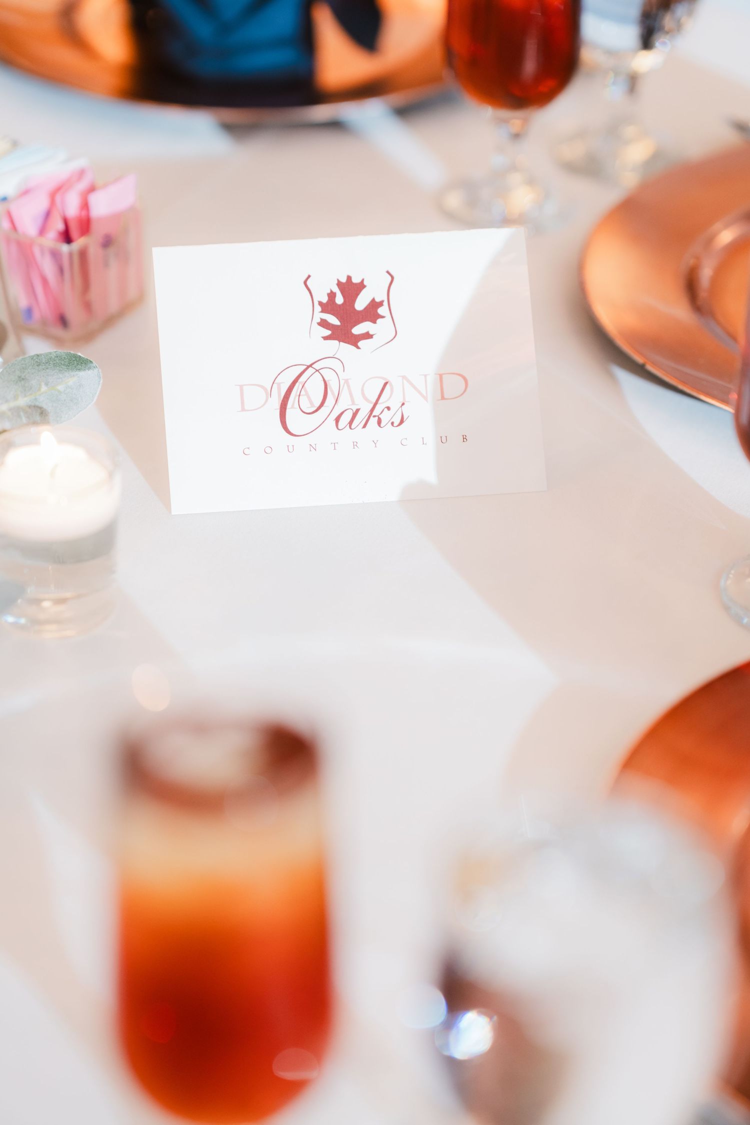 Place card with elegant red logo and text reading 'Oaks' on a formal dining table with glassware and plates.