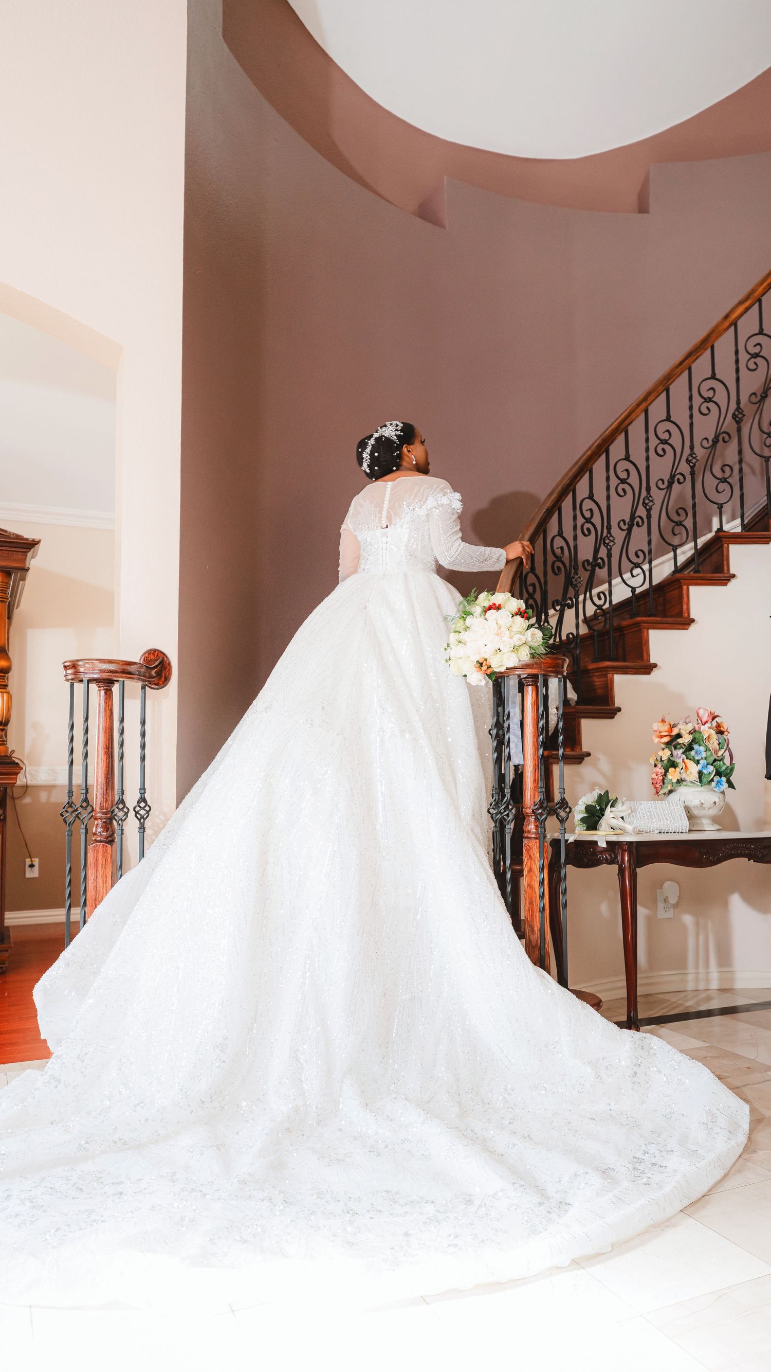 A stunning white wedding gown with a dramatic cathedral train photographed in an elegant interior staircase setting.