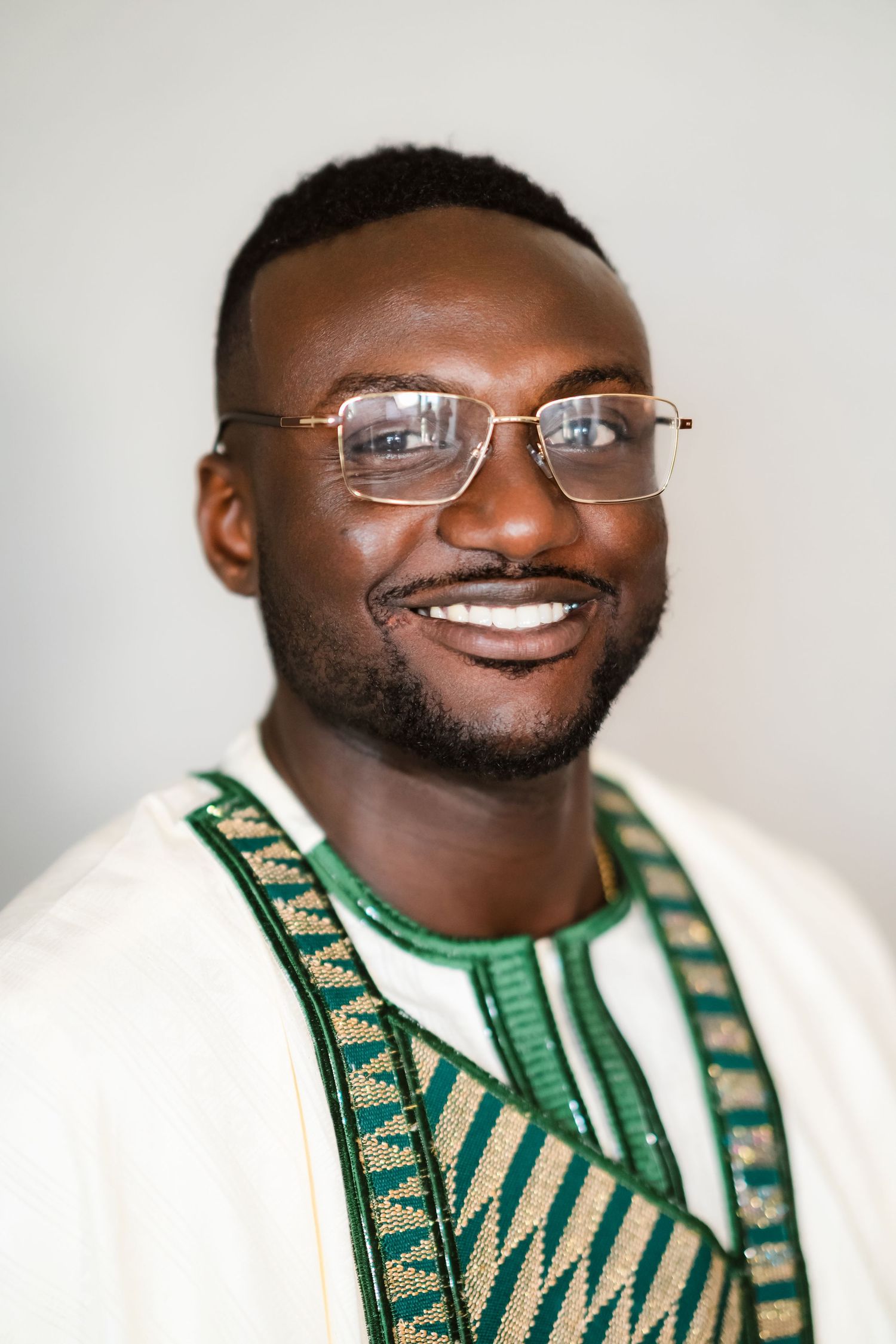 Portrait of a person wearing glasses and a traditional white and green embroidered outfit.