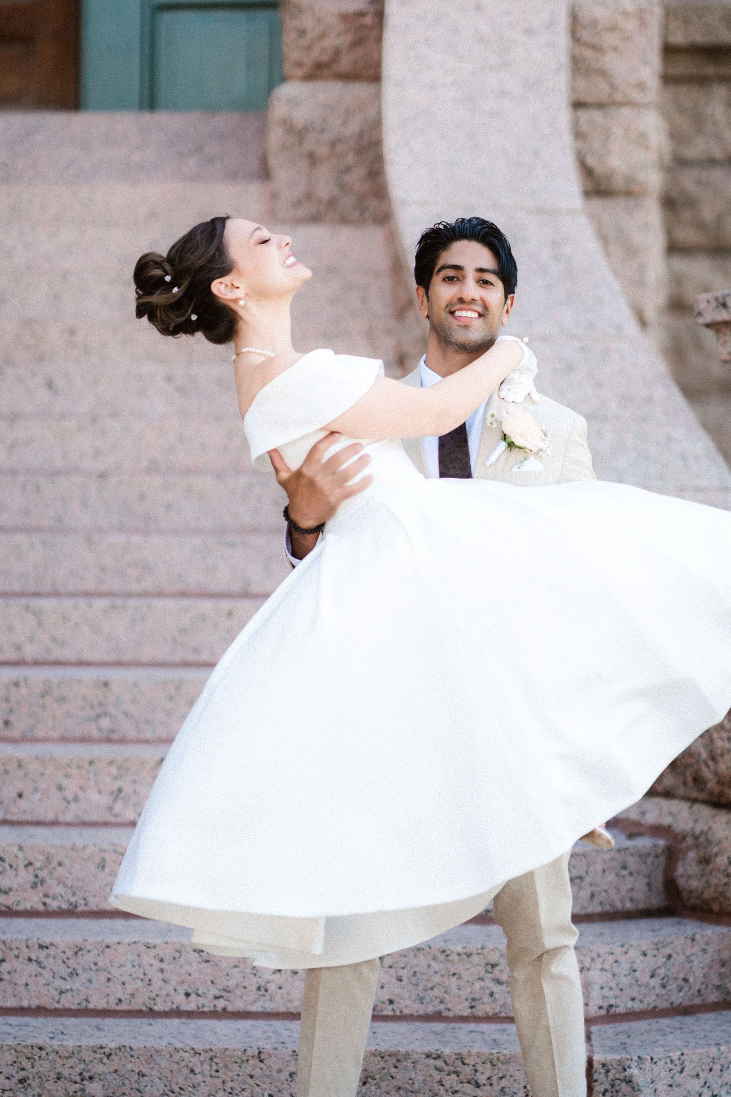A bride in a white dress twirls playfully on stone steps during a wedding photoshoot.