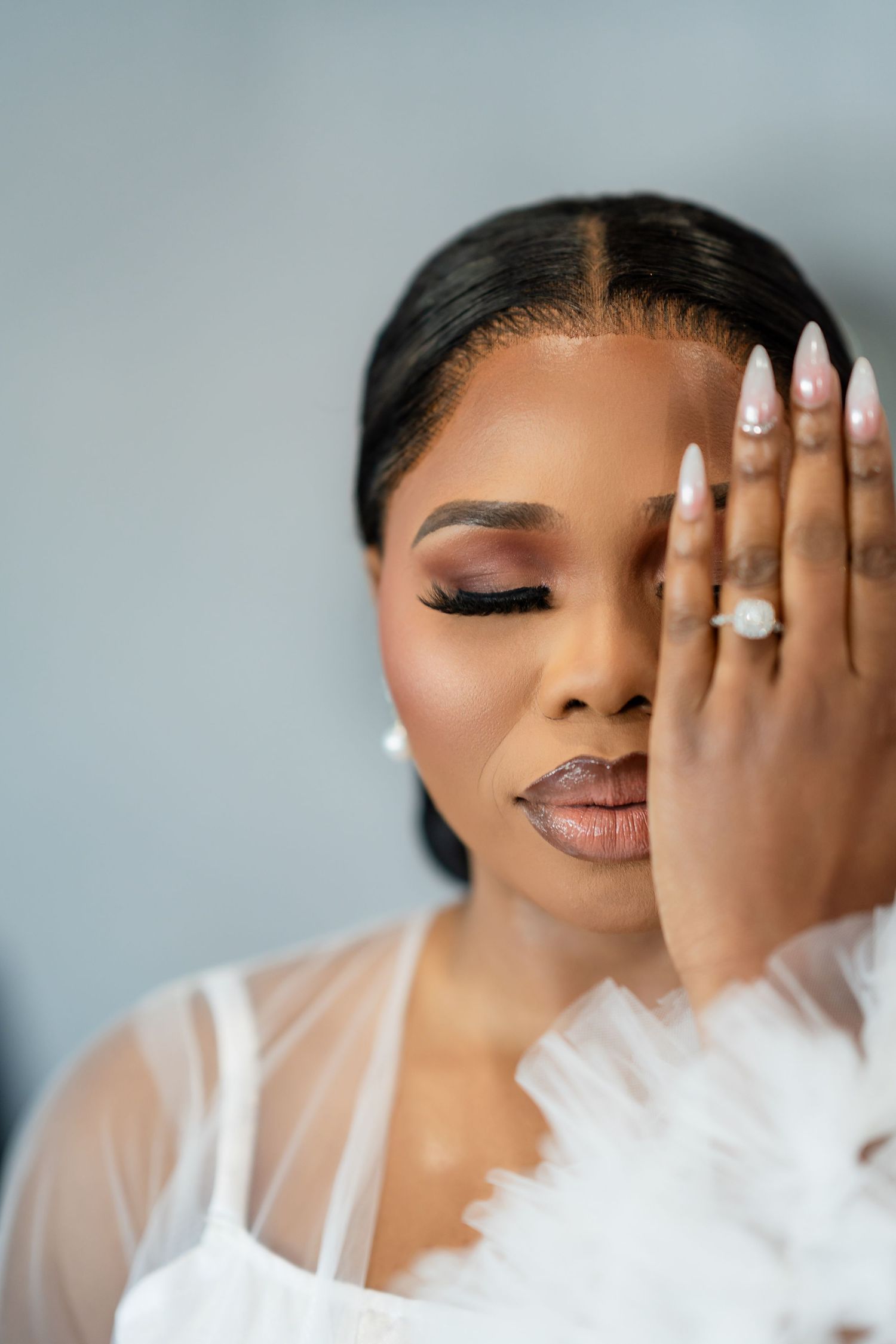 Elegant bridal beauty details showing ring, makeup and feathered white dress elements.