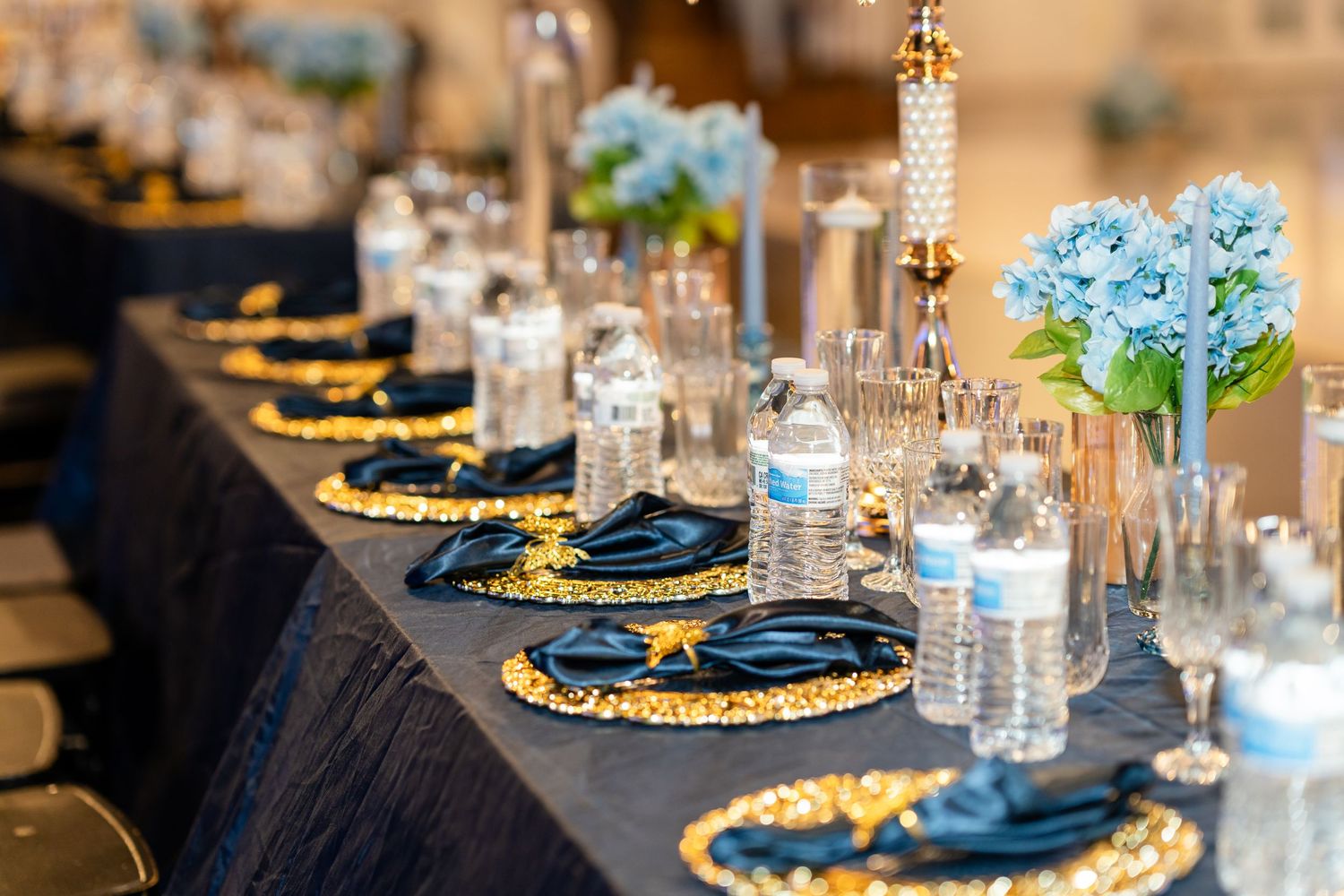 Elegant wedding table setting with gold chargers, navy napkins and blue hydrangeas.