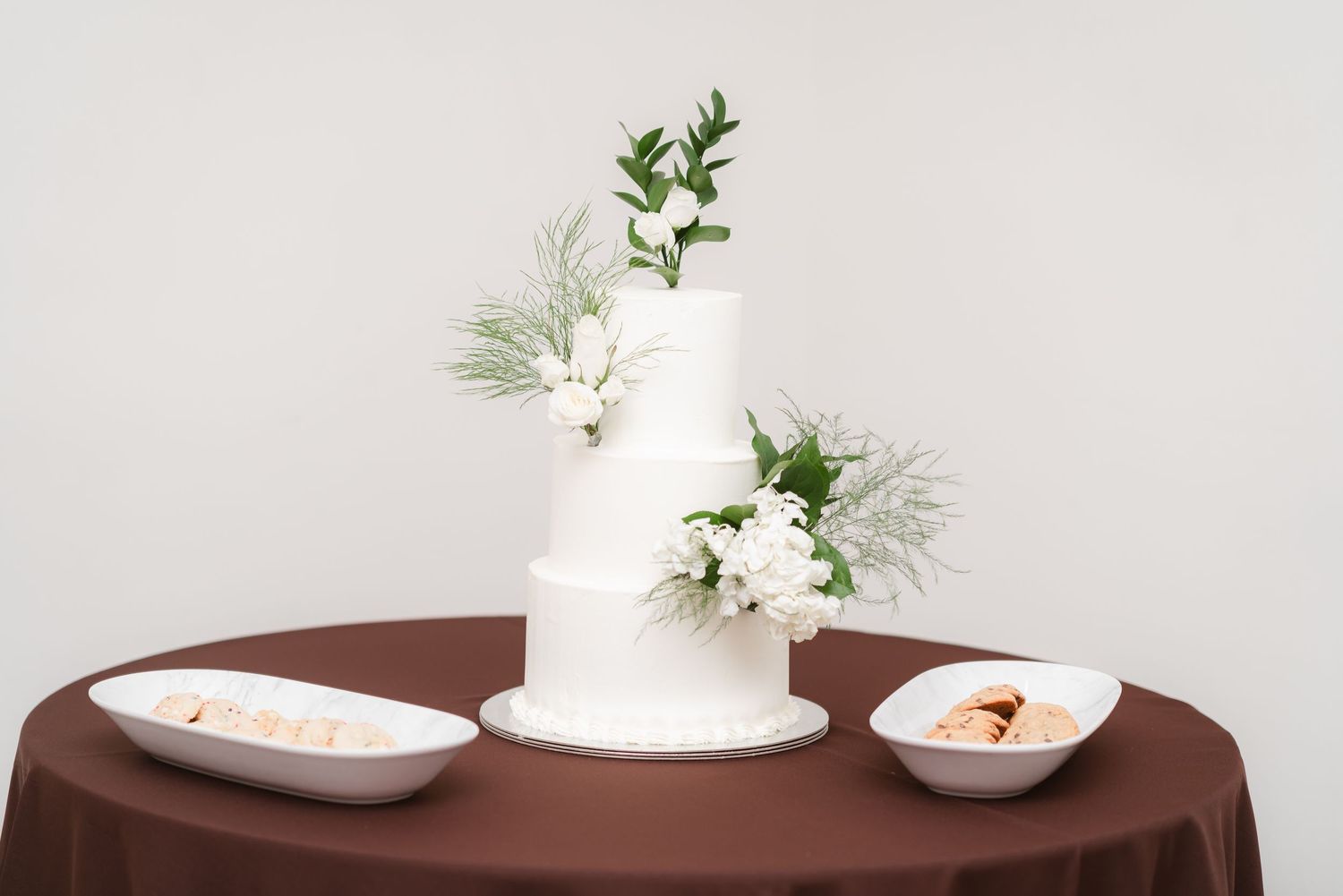White ceramic vases and floral arrangements displayed on a dark wood round table create an elegant minimalist centerpiece.