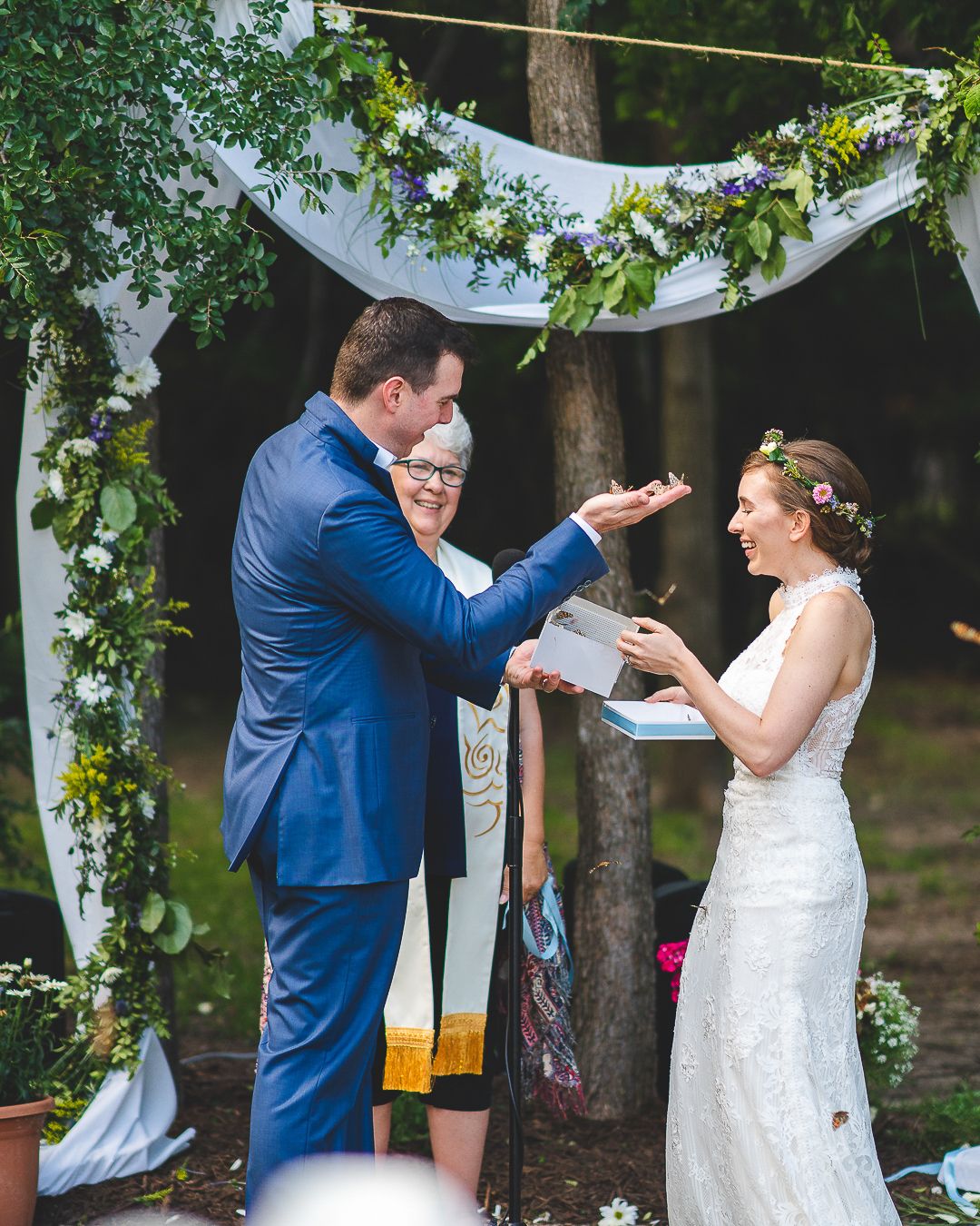 Wedding ceremony under a floral arch with white fabric and greenery decorations.