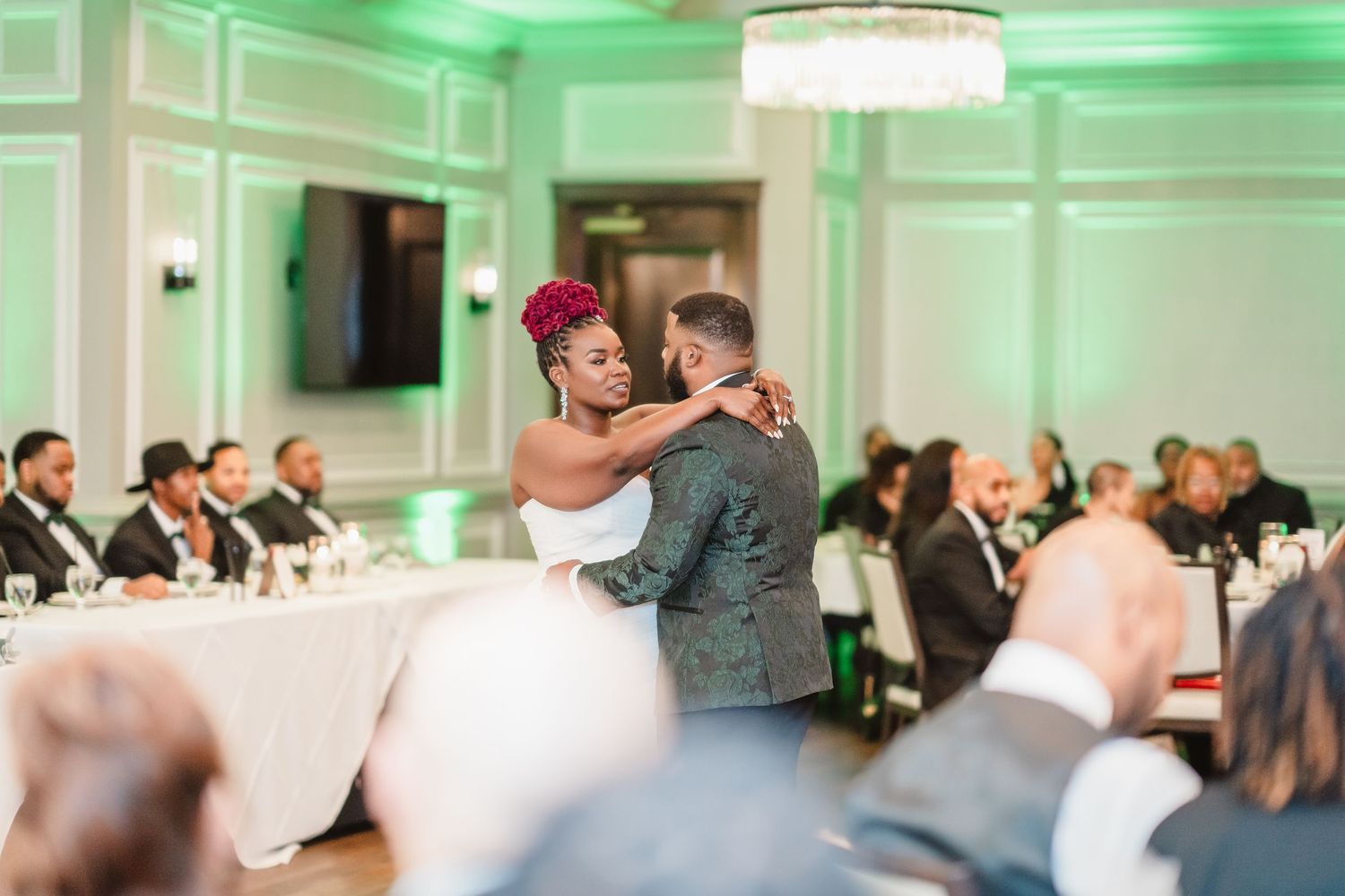Wedding couple shares their first dance in an elegant ballroom with green ambient lighting.