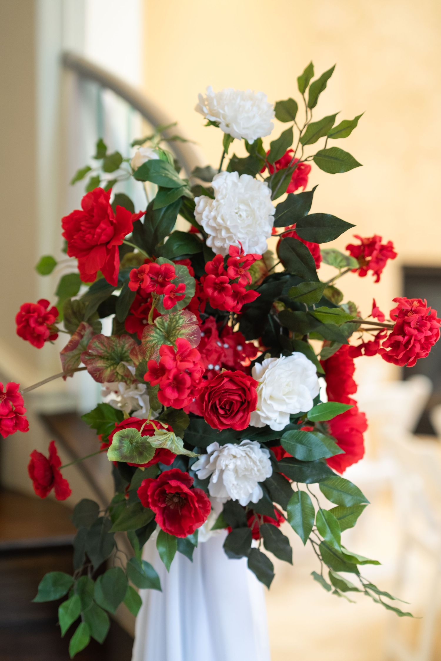 Elegant floral arrangement featuring red and white roses with green foliage in white vase.