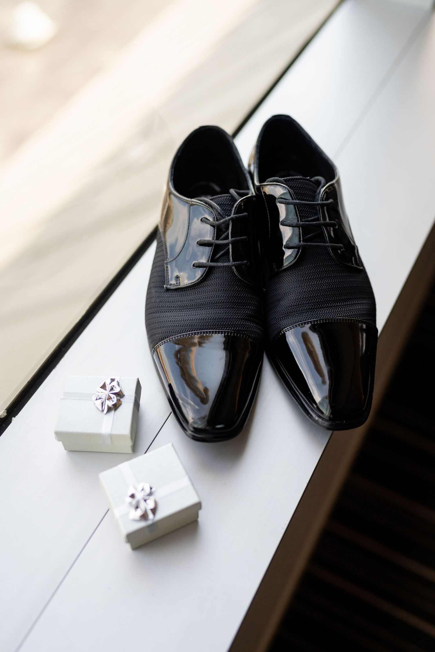 Formal black patent leather dress shoes with cufflinks displayed on white surface.