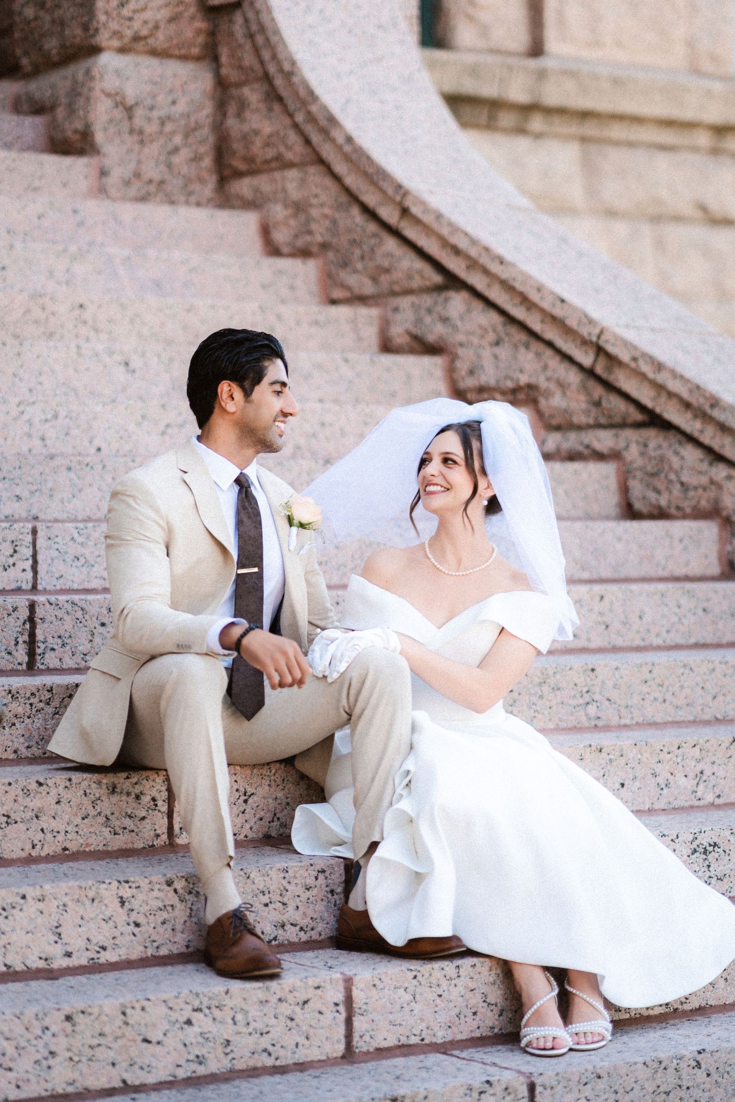 Romantic wedding couple sitting on stone steps in formal attire sharing intimate moments together.