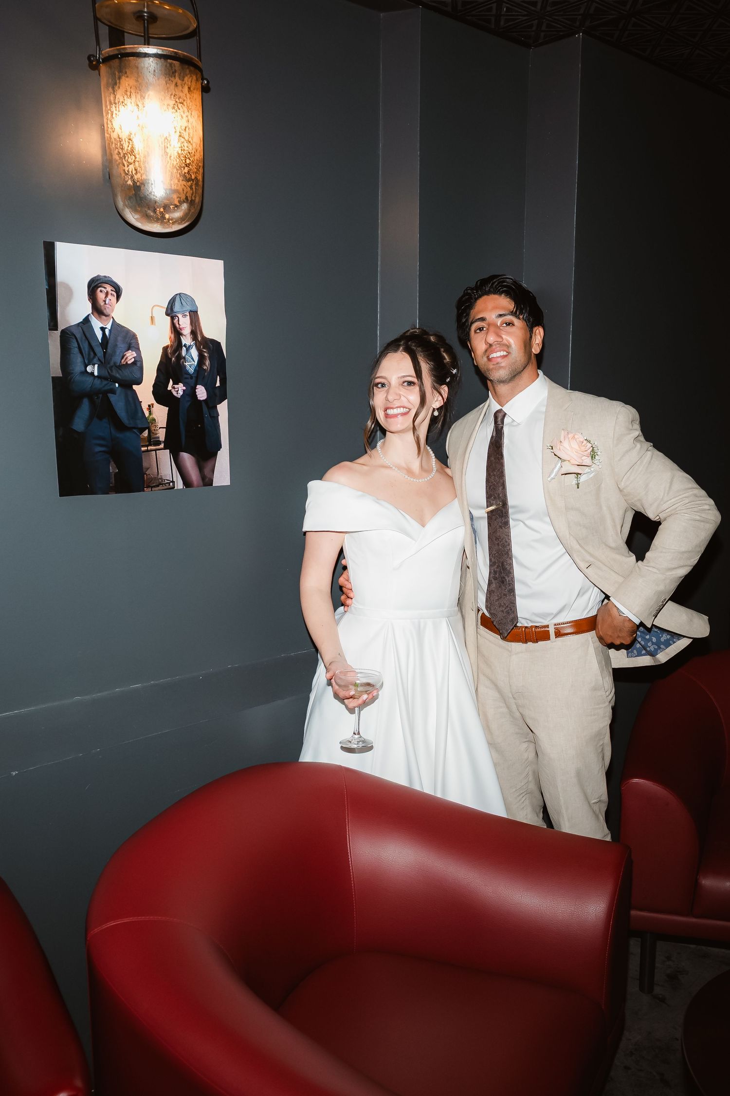 A couple in wedding attire poses in front of a framed photo in a dimly lit room.