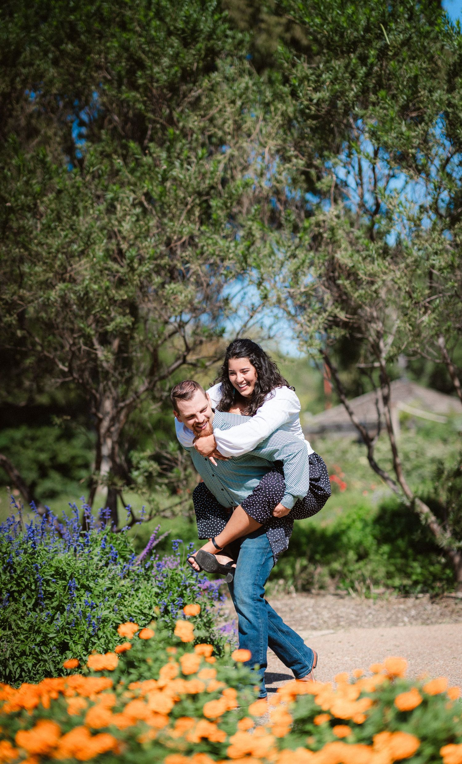 Playful couple poses among orange wildflowers and purple lupines in a natural outdoor setting.