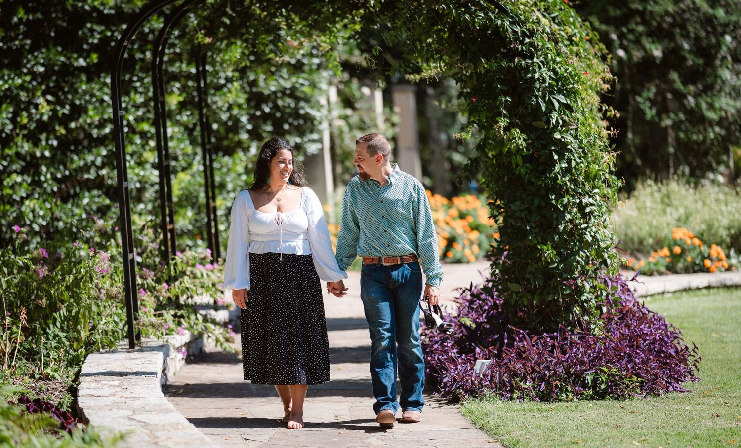 Two people walking together on a stone path surrounded by blooming gardens.