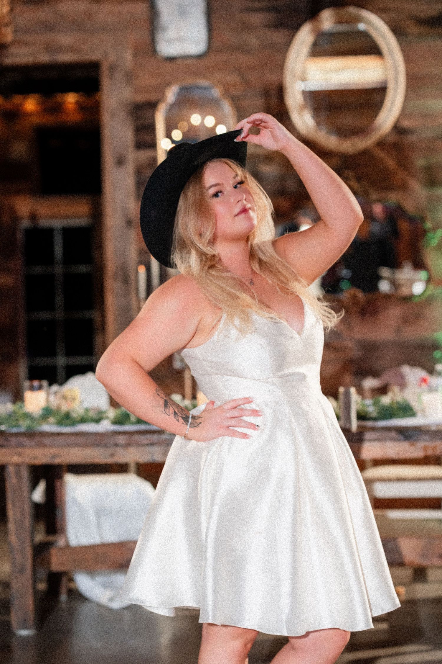A short white wedding dress being modeled in a rustic indoor venue with wooden walls.