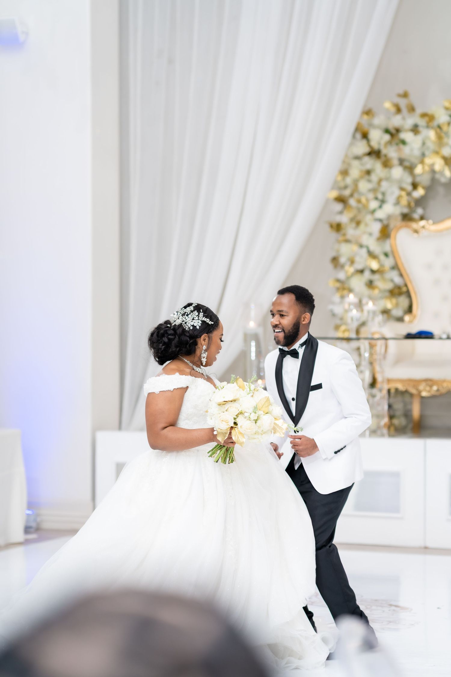 A wedding couple dancing together in an elegant white-draped reception venue with gold decor.