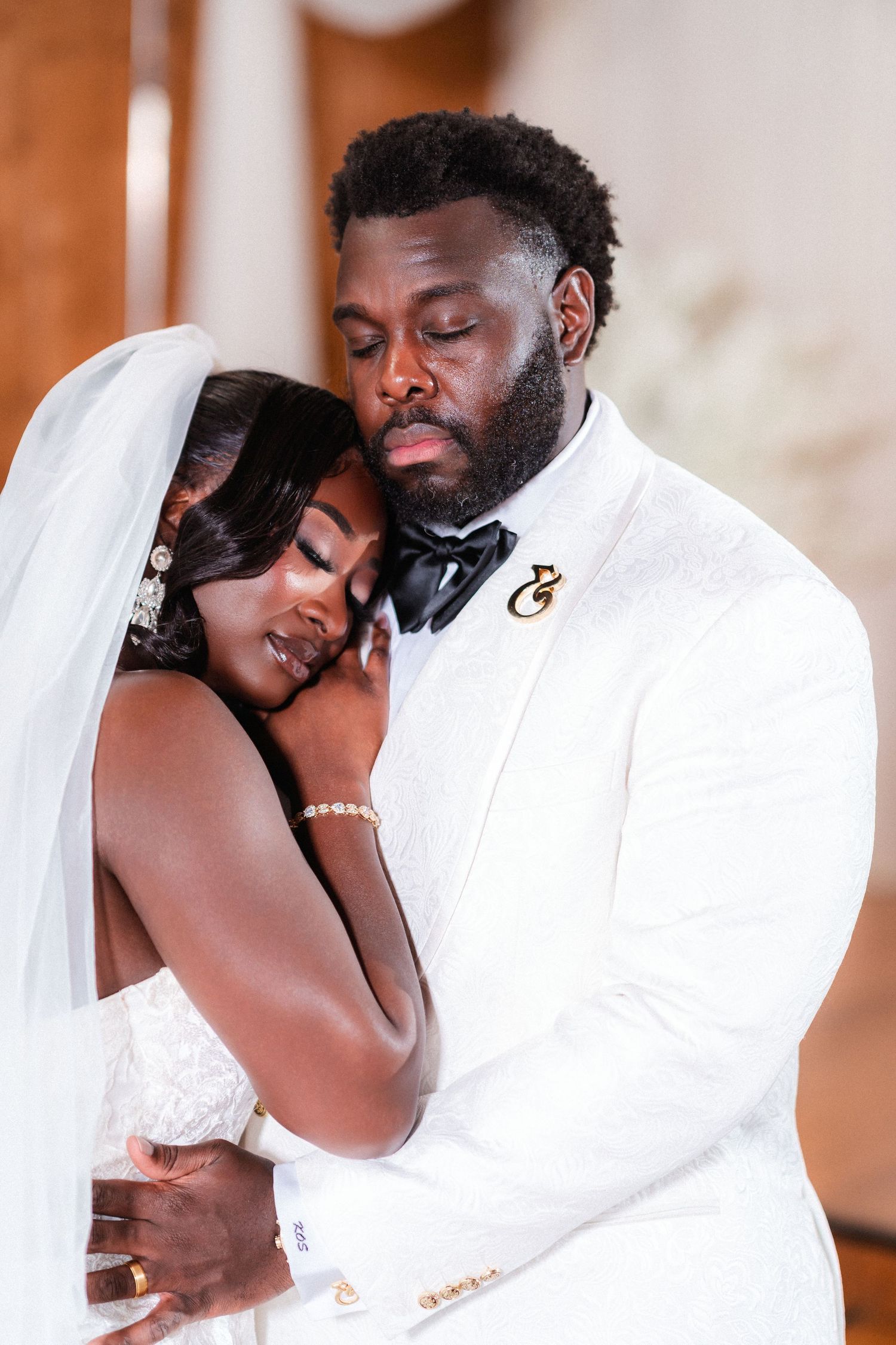 A tender embrace between newlyweds wearing white formal attire.