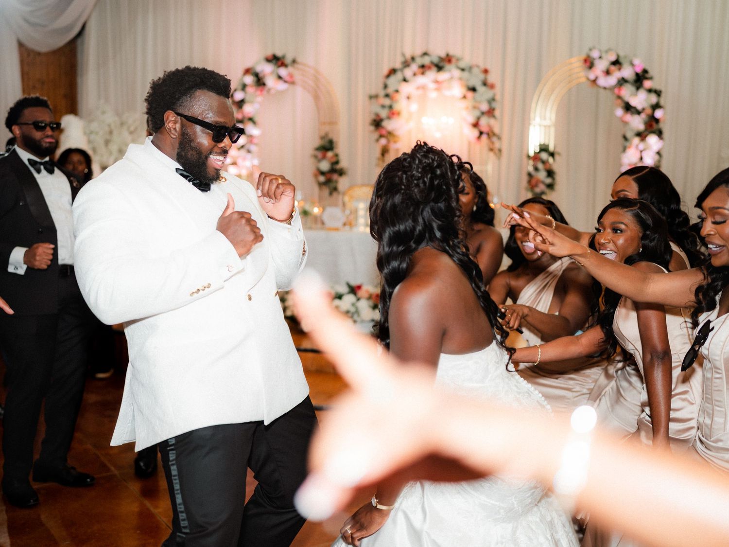 Wedding celebration with guests dancing and enjoying festivities under floral arch decorations.