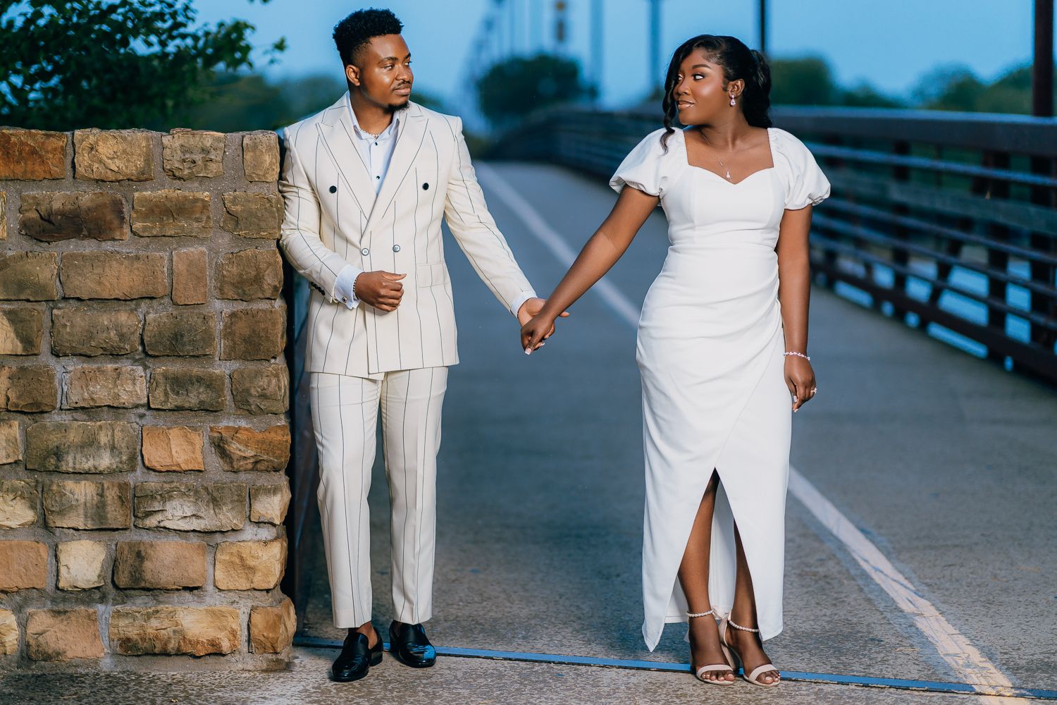 Couple in coordinated white outfits pose together on a brick-lined walkway.