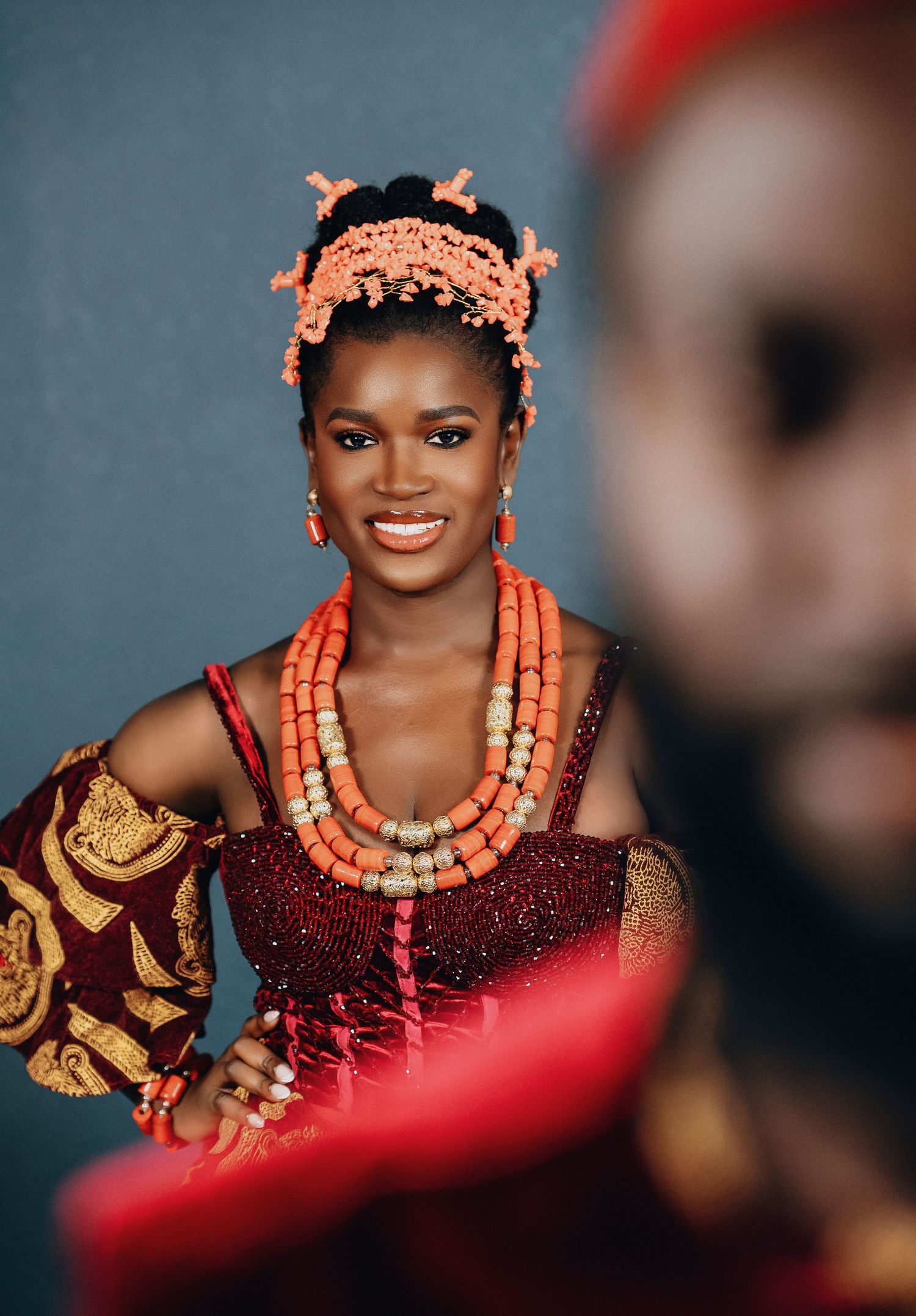 Close-up portrait showcasing coral beaded jewelry and traditional African wedding attire against grey backdrop.