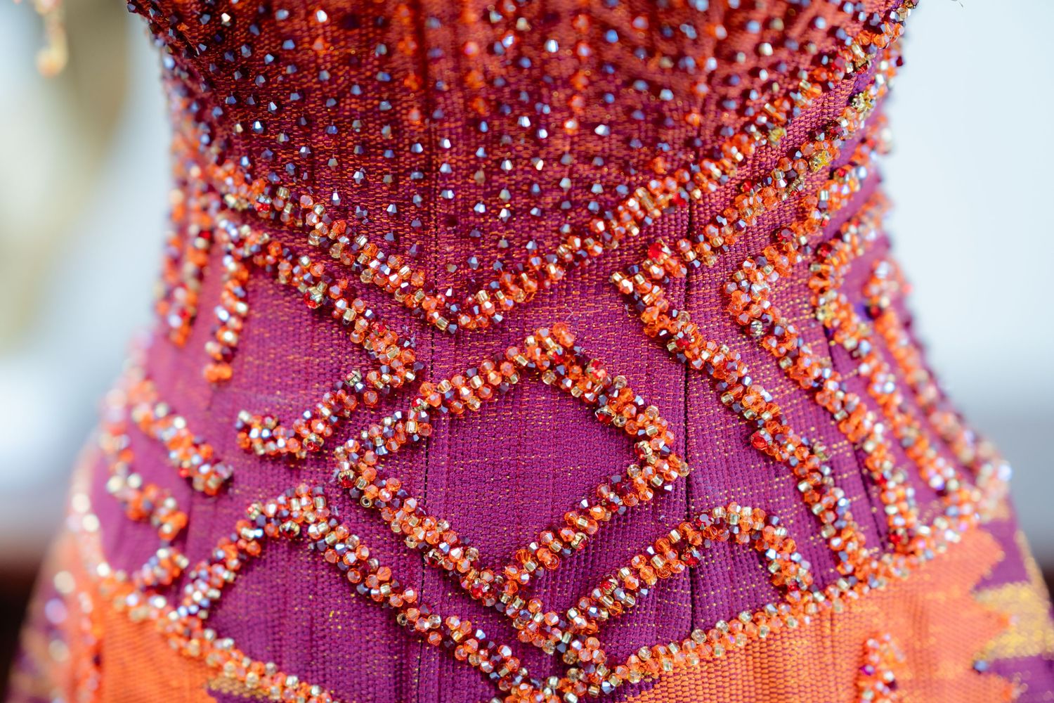 Detailed view of purple and coral beadwork pattern on formal dress fabric.