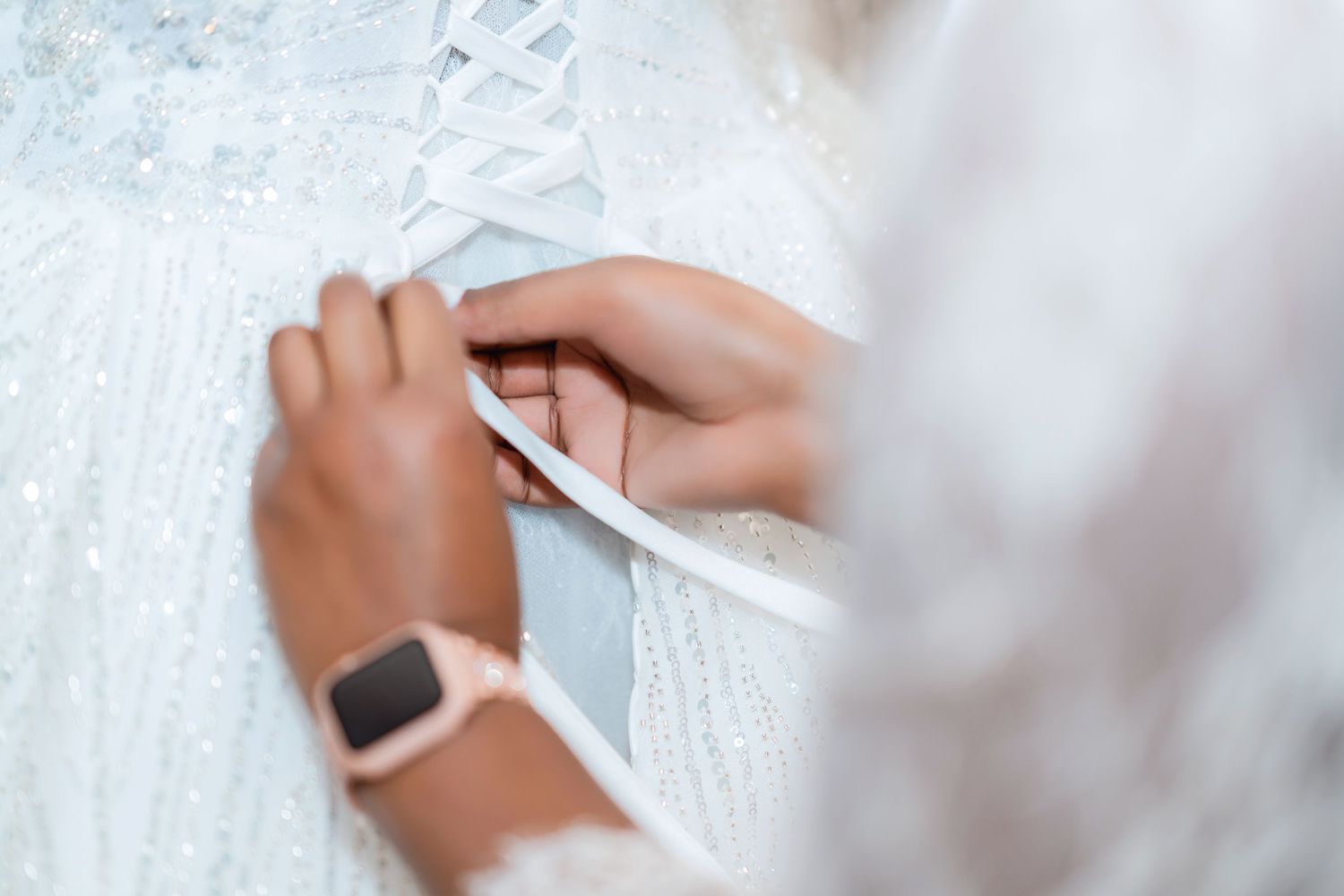 Close-up shot of hands adjusting white lace details on a wedding dress while wearing a smart watch.