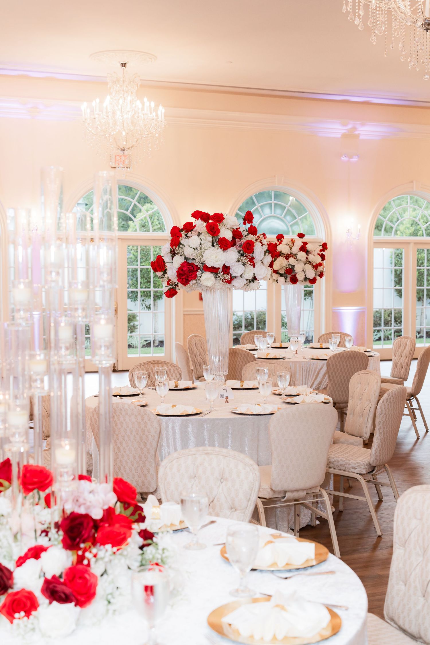 Luxurious wedding reception hall with red and white floral decor and crystal chandeliers.