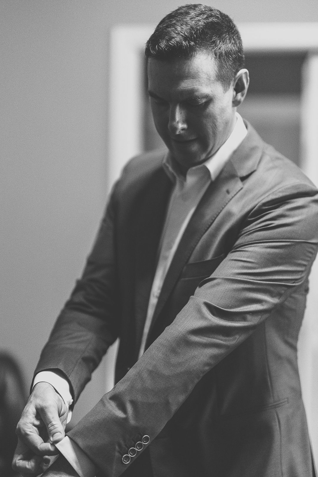 Black and white portrait of a person adjusting their suit jacket.