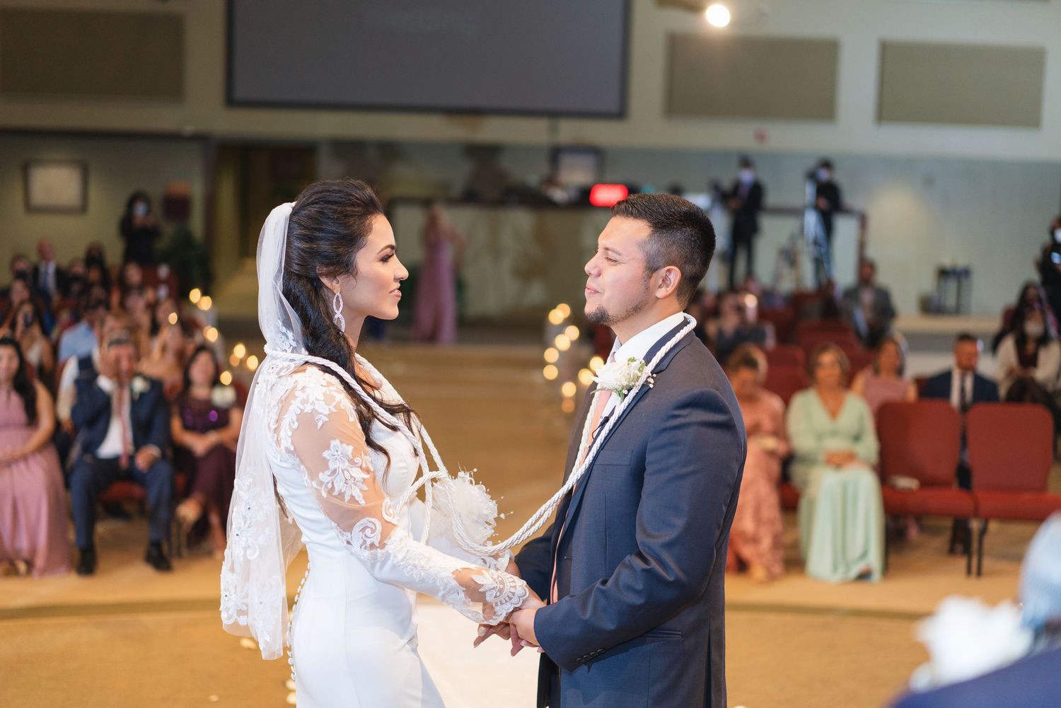 Wedding couple dancing together in a spacious reception hall filled with guests.