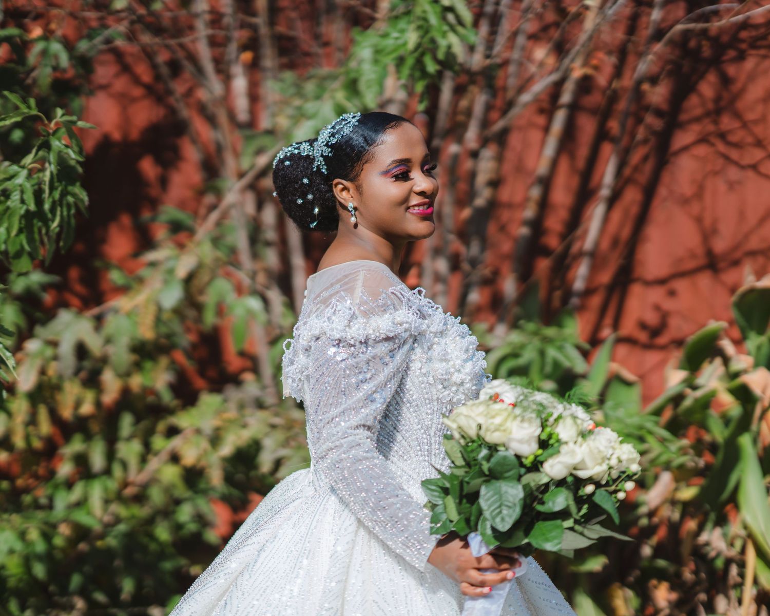 A beautiful bridal portrait showcasing an ornate white lace gown against a rustic red brick backdrop.