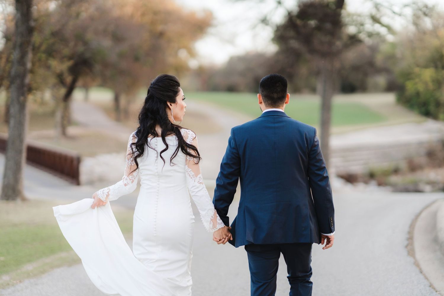 Couple walking together on a path surrounded by autumn trees and fallen leaves.