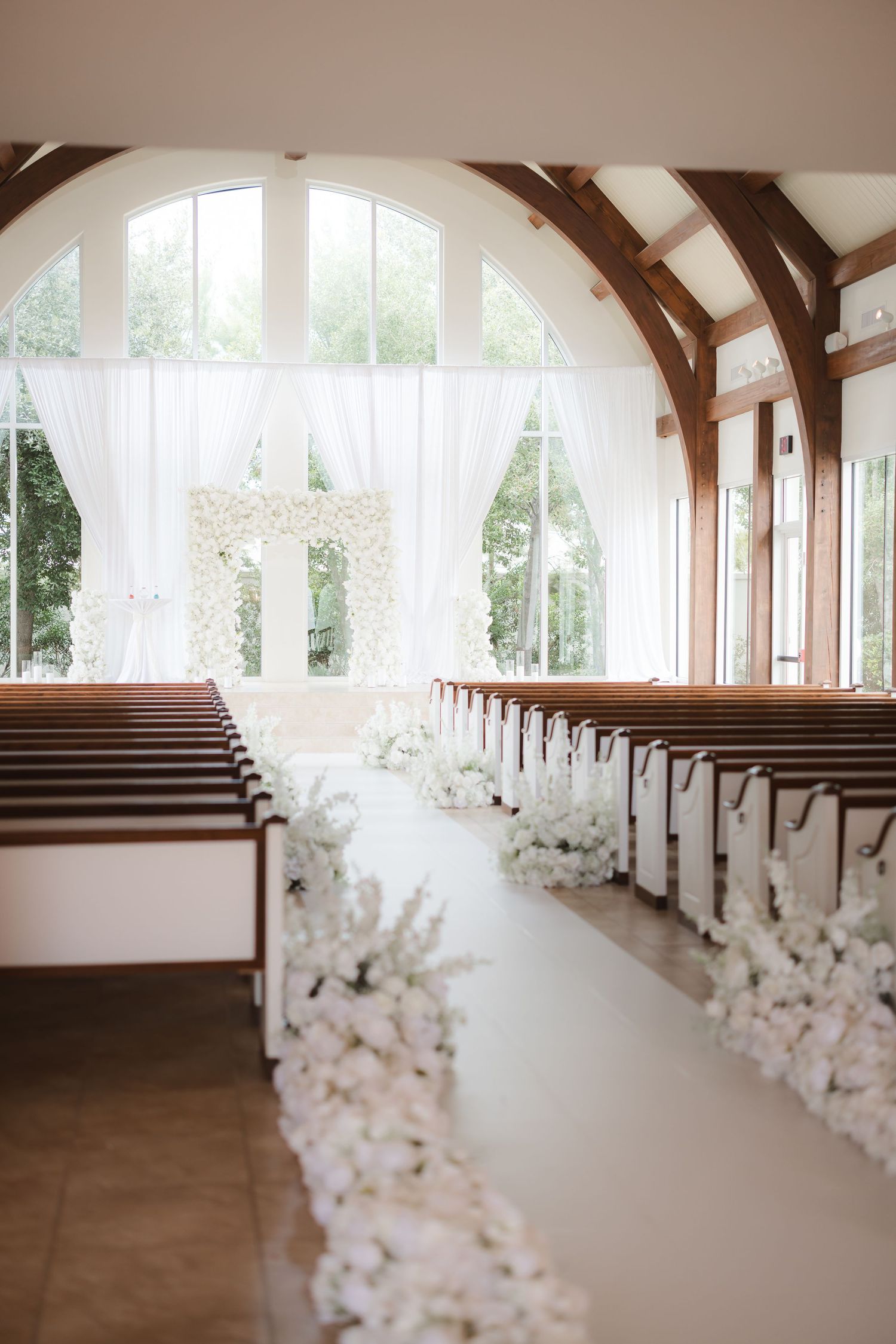 An elegant wedding chapel with wooden beams and white floral aisle decorations.