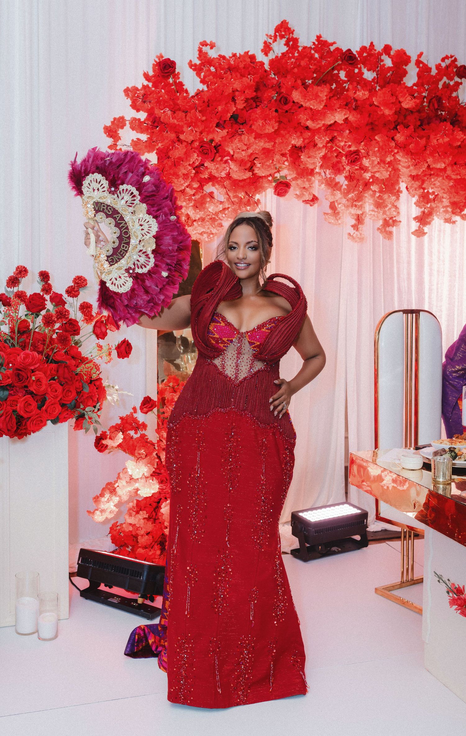A stunning red beaded gown with a sweetheart neckline photographed against a backdrop of vibrant red floral decorations.