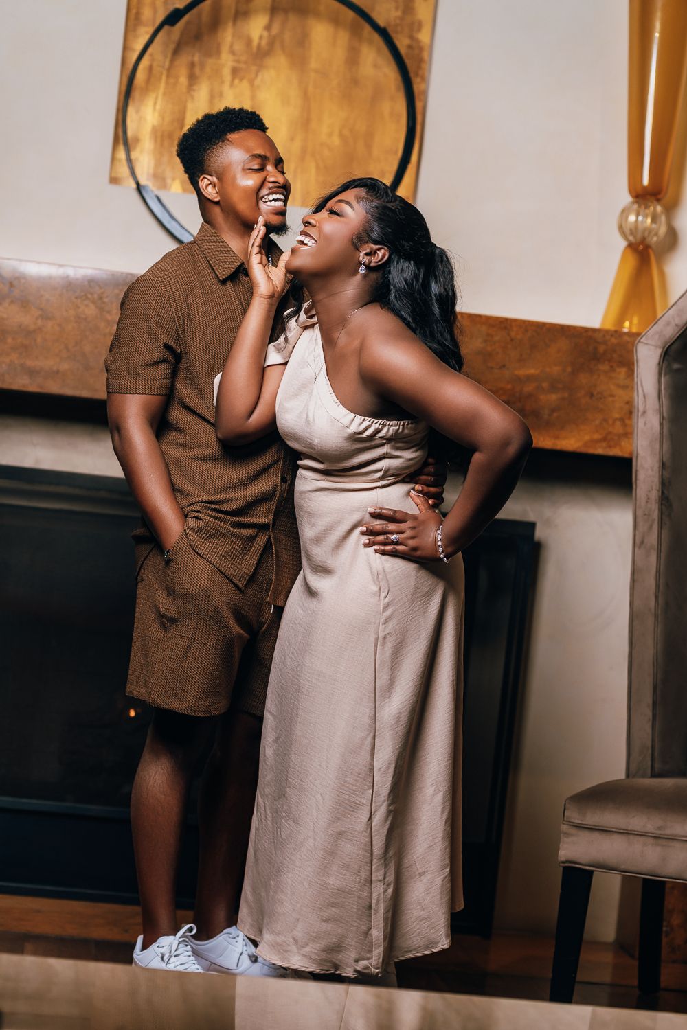 Couple in neutral tones share playful moments during indoor photoshoot with wooden backdrop.