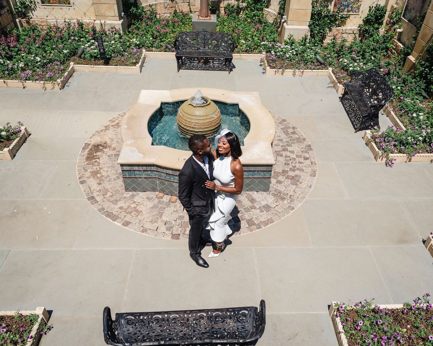 A formal couple's photo session on a stone pathway surrounded by brick walls and landscaping.