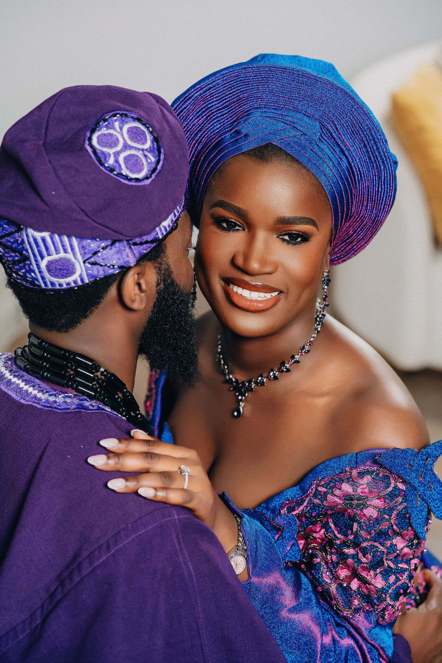 A couple in matching purple and blue traditional African attire share intimate moments in studio portraits.