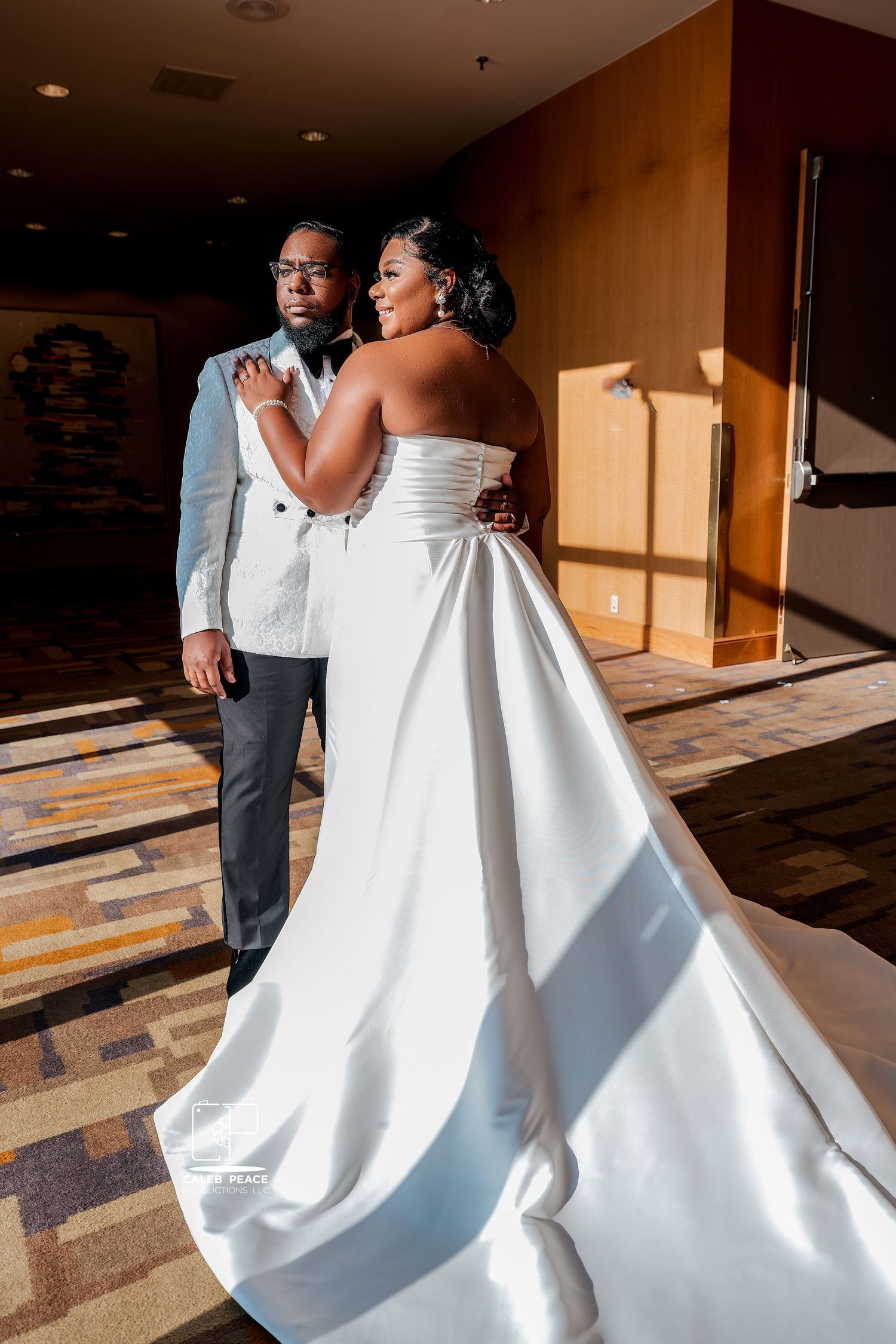 A couple in wedding attire poses in dramatic lighting, with the bride's white gown flowing elegantly.