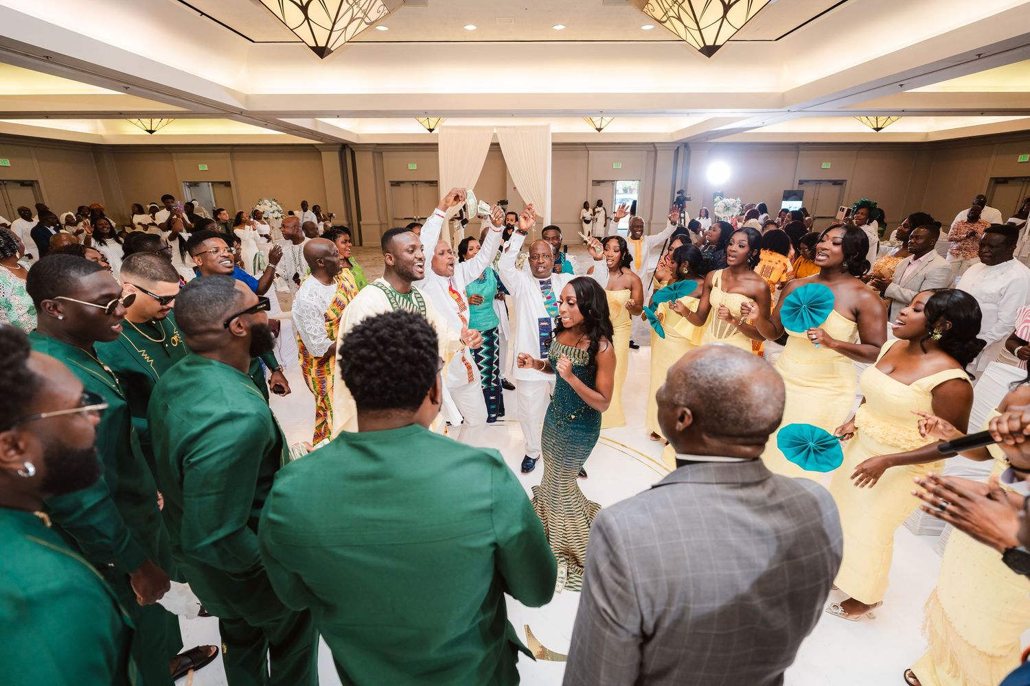 Wide view of wedding guests dancing and celebrating in a grand ballroom.