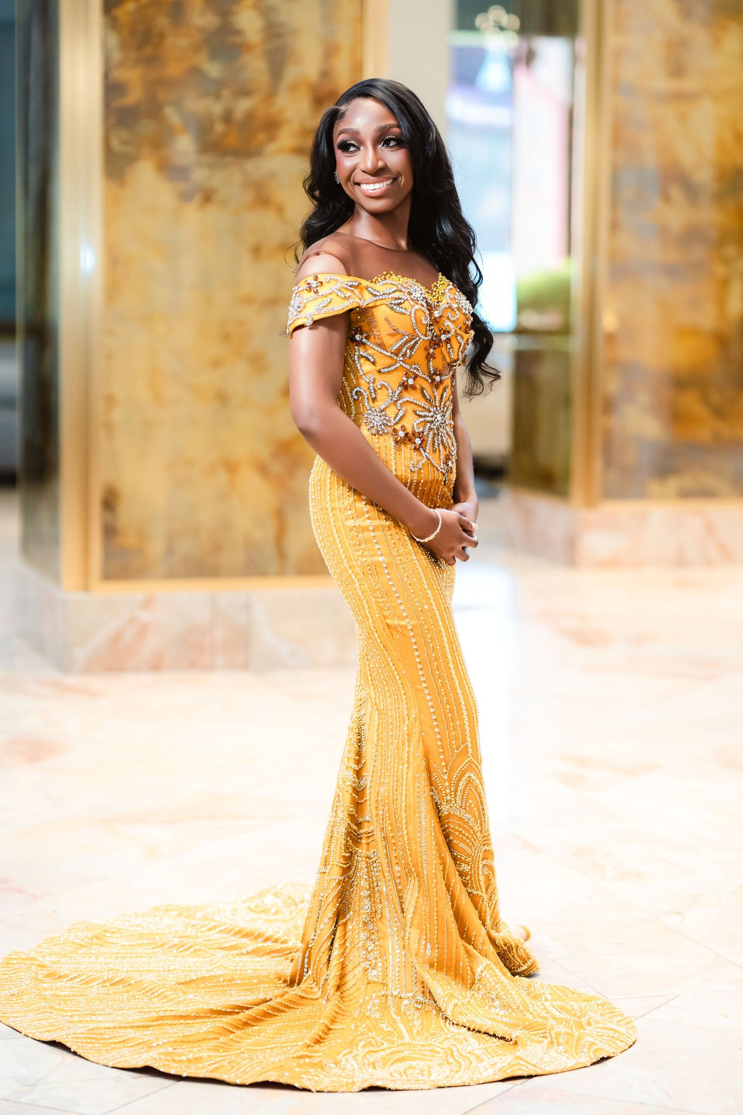 Stunning gold formal gown with intricate beading and a flowing train in an elegant setting.