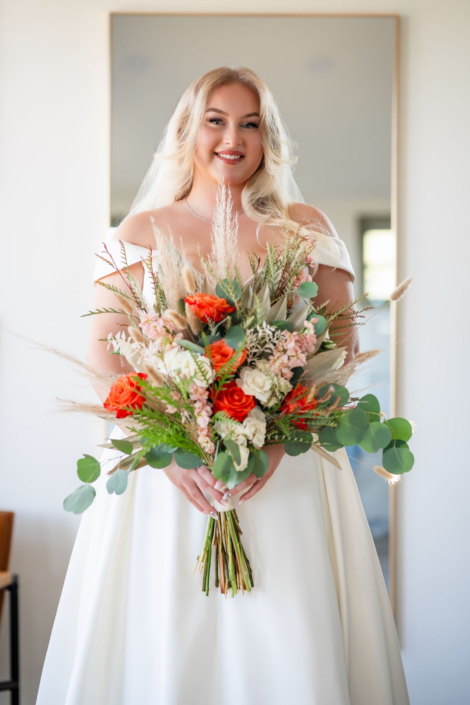 A bride in a white wedding dress holds a vibrant bouquet with orange roses and greenery.
