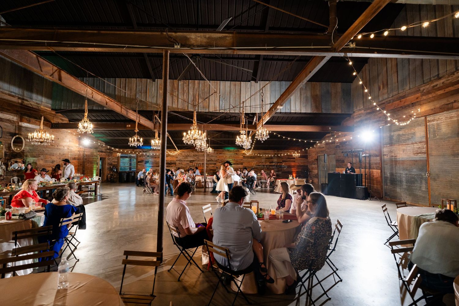 Panoramic view of a rustic barn reception venue with string lights and wooden beams.